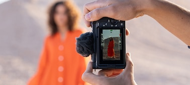 Imagen de uso de manos sosteniendo la cámara verticalmente y fotografiando a una modelo femenina, que se puede ver en la pantalla de la cámara